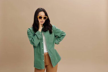 Şşş. Hakiki yeşil tişörtlü, heyecanlı Koreli genç kadın, dedikoduları bir yana bırakıp bej renkli pastel stüdyo arka planında yalnız poz veriyor. Güzel moda teklifi. Güneş gözlüğü reklam konsepti