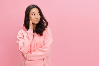 Harika, sevimli, neşeli, mutlu Asyalı öğrenci pembe kapüşonlu genç bayan pembe stüdyo arka planında yalnız poz veriyor. İyi bir teklif. Moda Yeni Koleksiyon Konsepti