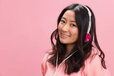 Pembe kapüşonlu, sevimli kulaklıklı sevimli, sevimli Asyalı bayan pembe stüdyo arka planında aşkla poz veriyor. İyi bir teklif. Ses yayını platform reklam kavramı