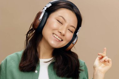 Bej renkli pastel stüdyo arka planında izole edilmiş yeşil kulaklıklı Koreli neşeli öğrenci kızın yakın plan portresi. Güzel moda teklifi. Müzik Uygulaması Platformu Reklam Konsepti