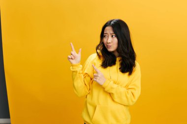 Düşünceli şüpheci Asyalı genç kız sarı kapüşonlu kazak içinde boş fotokopi odasında turuncu stüdyo arka planında yalnız poz vermek için poz veriyor. Güzel teklif. Halkın Duyguları kavramı