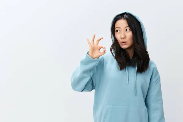可爱可爱可爱的亚洲年轻女性 穿着蓝色的连帽衫 展示出好的手势 在白色的工作室背景上摆出孤立的姿势 最好的广告报价 时装新品系列广告概念 — 图库照片