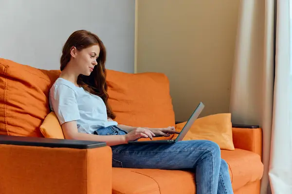 beautiful woman chatting on the orange couch with a laptop Lifestyle. High quality photo