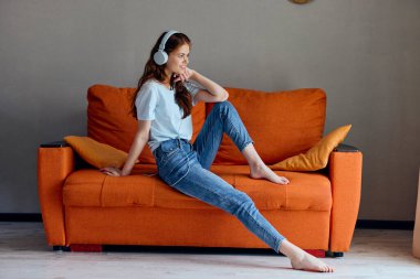 Portakal rengi koltukta kulaklıkla müzik dinleyen bir kadının portresi. Yüksek kalite fotoğraf