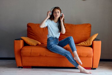 Portakal rengi koltukta kulaklıkla müzik dinleyen bir kadının portresi. Yüksek kalite fotoğraf