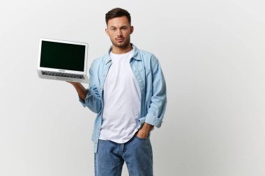 Dost canlısı, bronz tenli, sıradan, sıradan tişörtlü, elinde dizüstü bilgisayarla beyaz stüdyo arka planında yalnız poz veren yakışıklı bir bilişim uzmanı. Uzayın afiş modelini kopyala. Elektronik tamir konsepti