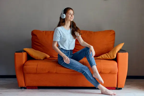 一个漂亮的女人 坐在橙色沙发上 用耳机听着音乐 毫无改动 高质量的照片 — 图库照片