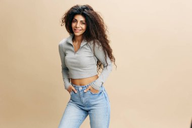 Havalı kotlar teklif ediyor. Afro saçlı, mutlu, seksi Latin kadın elini cebine atmış, kameraya bak. Moda. Pastel bej arka planda stüdyo çekimi. Boşluğu kopyala, tasarım reklamı için boş yer