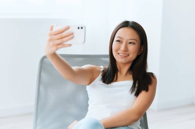 Neşeli, mutlu, bronzlaşmış, güzel, Asyalı bir kadın. Canlı yayında erkek arkadaşına gülümsüyor. Evde selfie videosu çekiyor. Mesafe iletişimi sosyal medya kavramı. Güzel teklif Banner Geniş açı