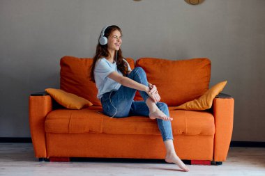 Turuncu kanepelerde kulaklıkla müzik dinleyen neşeli bir kadın. Yüksek kalite fotoğraf