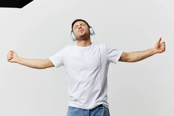 穿着T恤衫耳机 面色苍白的英俊男子听着最喜欢的歌曲 在白色的录音室背景上摆出孤身一人的样子跳舞 复制空间Banner模拟 音乐酷播放列表的概念 — 图库照片