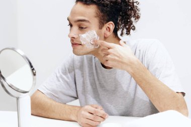 Aynalı cilt bakımının önünde beyaz tişörtlü genç bir adam görüldü. Yüksek kalite fotoğraf