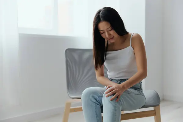 Cramp Broken Toe Broken Bone in Leg. Tormented suffering tanned beautiful young Asian woman touch leg at home interior living room. Injuries Poor health Illness concept. Cool offer Banner