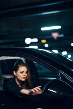 Yan taraftan, gece, arabada oturan, pencereden dışarı bakan ve elini dikiz aynasına uzatan bir kadının dikey fotoğrafı. Yüksek kalite fotoğraf