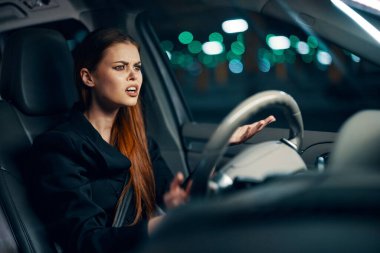 Bir kadının direksiyonda oturup gergin bir ifadeyle yola baktığı yatay bir fotoğraf. Geceleri fotoğrafçılık. Yüksek kalite fotoğraf