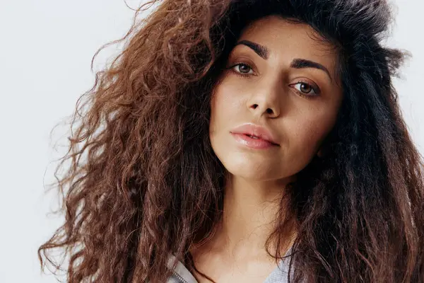 Seksi kıvırcık kıvırcık Latin kadın kameraya bakıyor ve sana gülümsüyor, stüdyoda izole beyaz arka plan pozu veriyor. Moda ve kozmetik markaları için iyi bir teklif. Reklam için portreyi kapat 