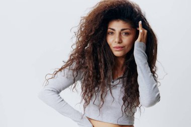 Beyaz Stüdyo Duvarı 'nda izole edilmiş, Kıvırcık Saçlı, Gri Süveterli Güzel Latin Kadın Görünüşü. Moda Mevsimsel Satış Yeni Koleksiyon Sevgi Kendini Kavrama