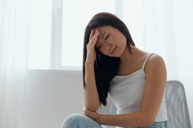 Migrenim tuttu. Evdeki oturma odasında alnına dokunan bronzlaşmış güzel Asyalı kadın yüzünden acı çeken mutsuz bir portre. Yaralar Kötü Sağlık Hastalığı konsepti. Güzel teklif Banner.