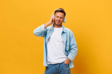 Mavi tişörtlü, mutlu, bronz tenli, yakışıklı adam kulaklıklı turuncu sarı stüdyo arka planında izole edilmiş havalı bir şarkıyla eğleniyor. Uzayın afiş modelini kopyala. Rahatlama zamanı konsept