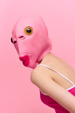 Yüzünde balık kafası olan pembe Cadılar Bayramı kostümü giymiş sıska bir kadın pembe arka planda komik bir poz veriyor ve kameraya bakıyor, sanat konsepti fotoğrafı. Yüksek kalite fotoğraf