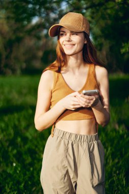 Genç bir kadın telefonu elinde duruyor ve doğada gün ışığında gülümsüyor. Bağımsız Yaşam Tarzı. Yüksek kalite fotoğraf