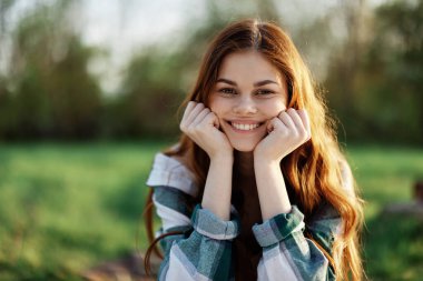 Yeşil bir parkta güzel bir kadın gün batımında kameraya bakıp güler ve gülümser. Yakın plan portre. Yüksek kalite fotoğraf