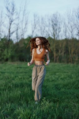 Yeşil pantolonlu ve spor ayakkabılı genç bir kadın saçı açık yeşil çimlerde koşuyor. Yüksek kalite fotoğraf