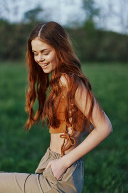 Doğadaki yeşil çimlerin üzerinde uzanan ve güzel bir gün batımını izlerken gülümseyen genç bir kadın. Yüksek kalite fotoğraf