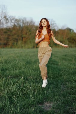 Bir kadın spor yapıyor ve parktaki tarlada koşuyor. Neşeli bir gülümsemeyle etrafındaki güzel yaz doğasına bakıyor. Yüksek kalite fotoğraf