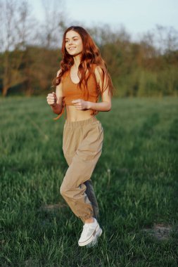 Bir kadın spor yapıyor ve parktaki tarlada koşuyor. Neşeli bir gülümsemeyle etrafındaki güzel yaz doğasına bakıyor. Yüksek kalite fotoğraf