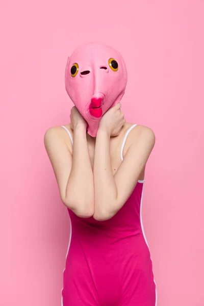 Woman in a fish costume for Halloween poses against a pink background in a crazy scary costume with a pink silicone mask on her head. High quality photo
