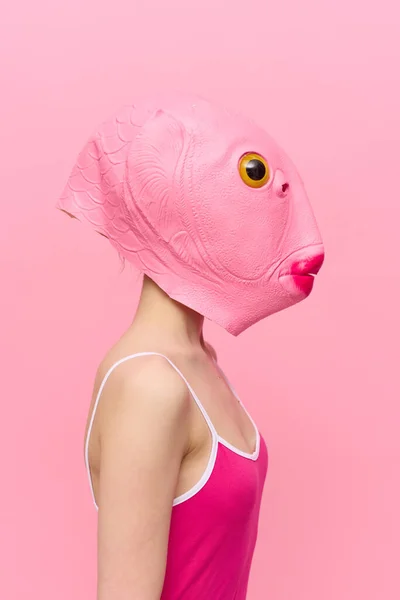 Funny crazy woman on a pink background standing in a fish head mask on a pink background, conceptual Halloween costume art photo. High quality photo