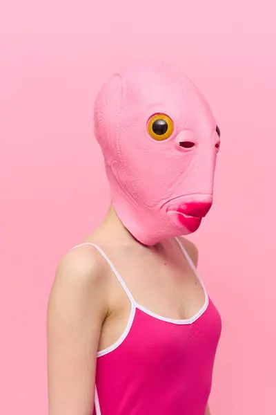 Funny crazy woman on a pink background standing in a fish head mask on a pink background, conceptual Halloween costume art photo. High quality photo