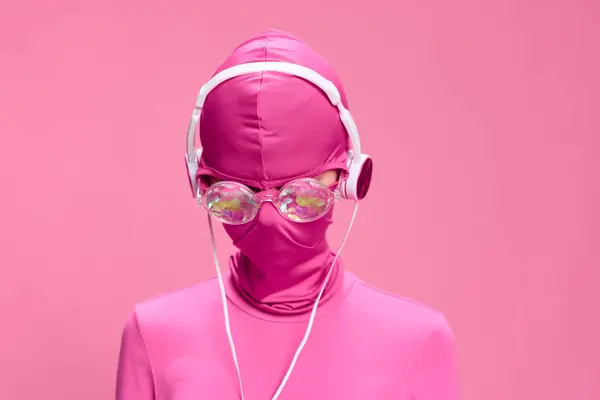 一个戴着粉色全脸防盗面具 戴着闪闪发光的圆形眼镜 戴着粉色耳机 粉色背景的女人的艺术肖像 高质量的照片 — 图库照片