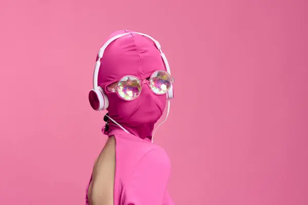 若い女性のサイバーパンクブロガーのクリエイティブファンアート写真は 丸い眼鏡とヘッドフォンを輝かせたピンクのフルフェイスマスクを着用したピンクの背景にあります 高品質の写真 — ストック写真