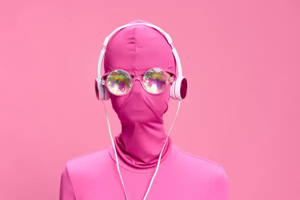一个戴着粉色全脸防盗面具 戴着闪闪发光的圆形眼镜 戴着粉色耳机 粉色背景的女人的艺术肖像 高质量的照片 — 图库照片