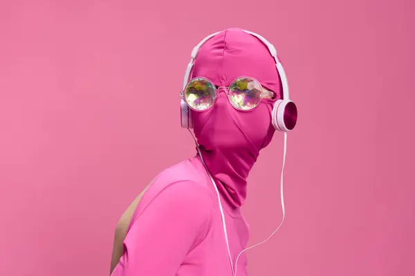 若い女性のサイバーパンクブロガーのクリエイティブファンアート写真は 丸い眼鏡とヘッドフォンを輝かせたピンクのフルフェイスマスクを着用したピンクの背景にあります 高品質の写真 — ストック写真