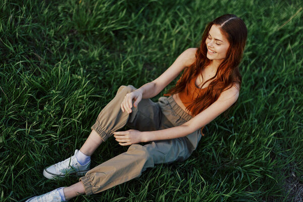 Freelance woman sitting in a park in summer on the grass looking at the sunset, sunshine in nature. High quality photo