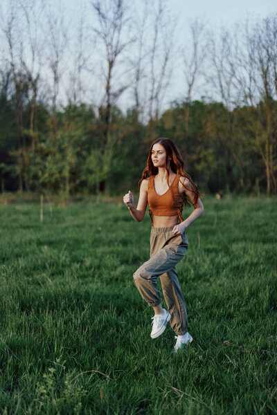 A young woman exercising outside and running in the park. in the evening on the green grass into the sunset. High quality photo