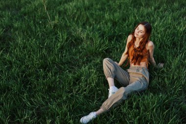 Bir kız parkta çimlerin üzerinde oturur ve yaz günbatımının güzel manzarasının tadını çıkarır. Yüksek kalite fotoğraf