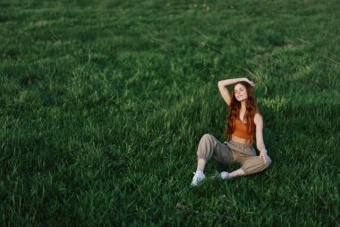Rahat giysiler içindeki bir kız parkta yürüdükten sonra çimlere oturdu meditasyon yapmak ve gün ışığında dinlenmek için. Yüksek kalite fotoğraf