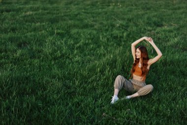 Rahat giysiler içindeki bir kız parkta yürüdükten sonra çimlere oturdu meditasyon yapmak ve gün ışığında dinlenmek için. Yüksek kalite fotoğraf
