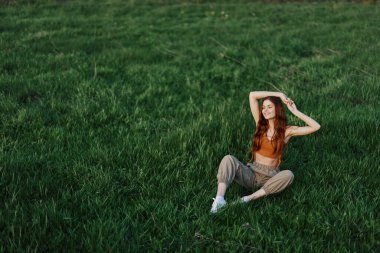 Rahat giysiler içindeki bir kız parkta yürüdükten sonra çimlere oturdu meditasyon yapmak ve gün ışığında dinlenmek için. Yüksek kalite fotoğraf