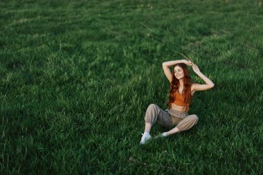 Rahat giysiler içindeki bir kız parkta yürüdükten sonra çimlere oturdu meditasyon yapmak ve gün ışığında dinlenmek için. Yüksek kalite fotoğraf