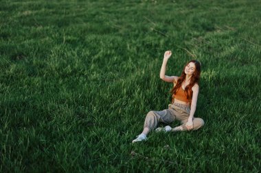 Serbest çalışan kız öğrenci parkta çimlerin üzerinde oturur ve günbatımını izler, dünya ve doğa ile uyum kavramını. Yüksek kalite fotoğraf