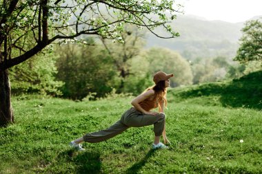 Genç bir atletik kadın parkta spor esneme hareketleri yapıyor. Yeşil yaz manzarası doğada güneş ışığı altında. Yüksek kalite fotoğraf