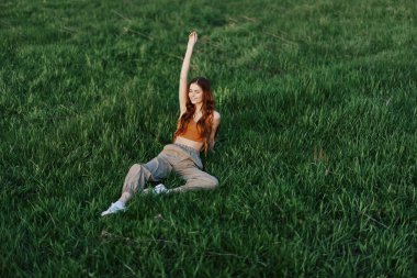 Serbest çalışan kız öğrenci parkta çimlerin üzerinde oturur ve günbatımını izler, dünya ve doğa ile uyum kavramını. Yüksek kalite fotoğraf