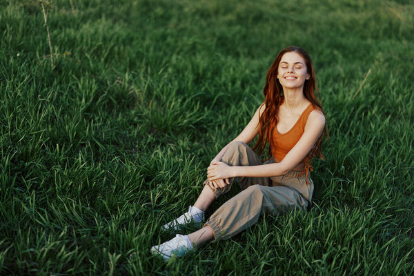 Lifestyle summer women on vacation in the park sitting on the green grass looking at the camera and smiling. High quality photo