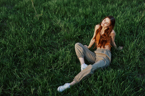 A girl sits on the grass in the park and enjoys the beautiful view of the summer sunset. High quality photo