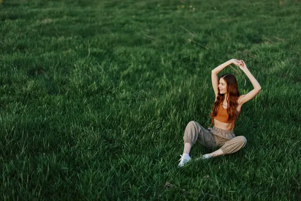 A girl in comfortable clothes sat on the grass after a walk in the park to meditate and rest in the sunlight. High quality photo